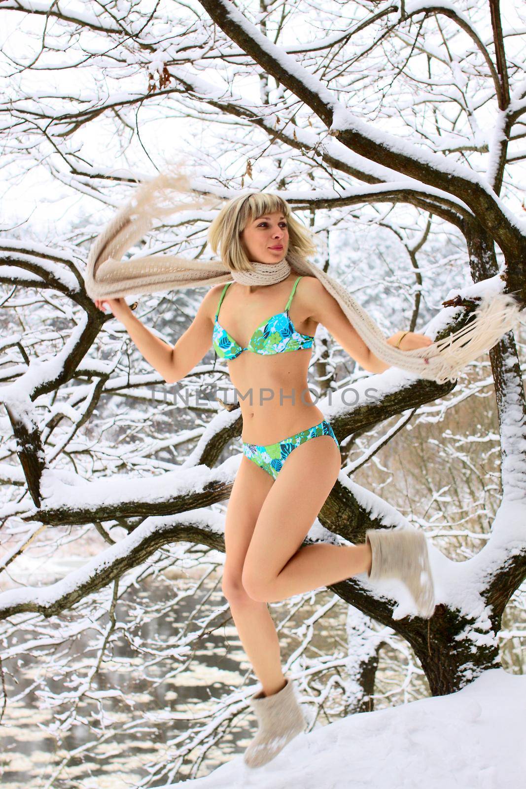 Blonde woman jumping on the snow in winter forest
