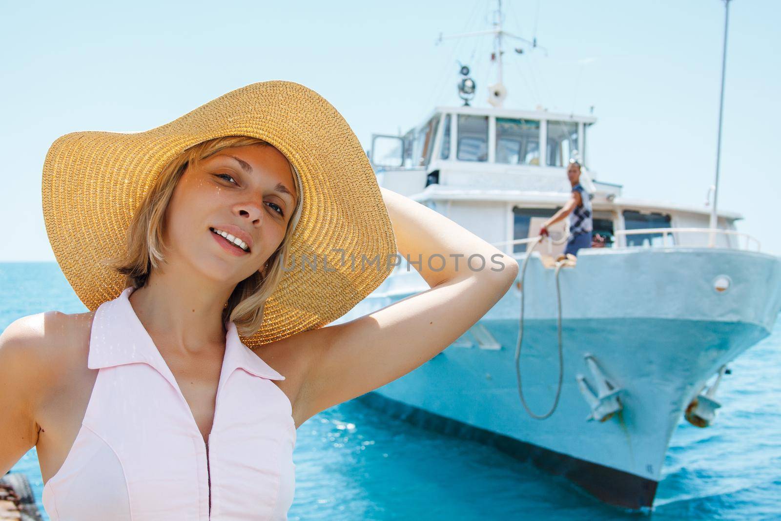 Smiling blonde attractive woman posing in hat. Ship on the sea on background.