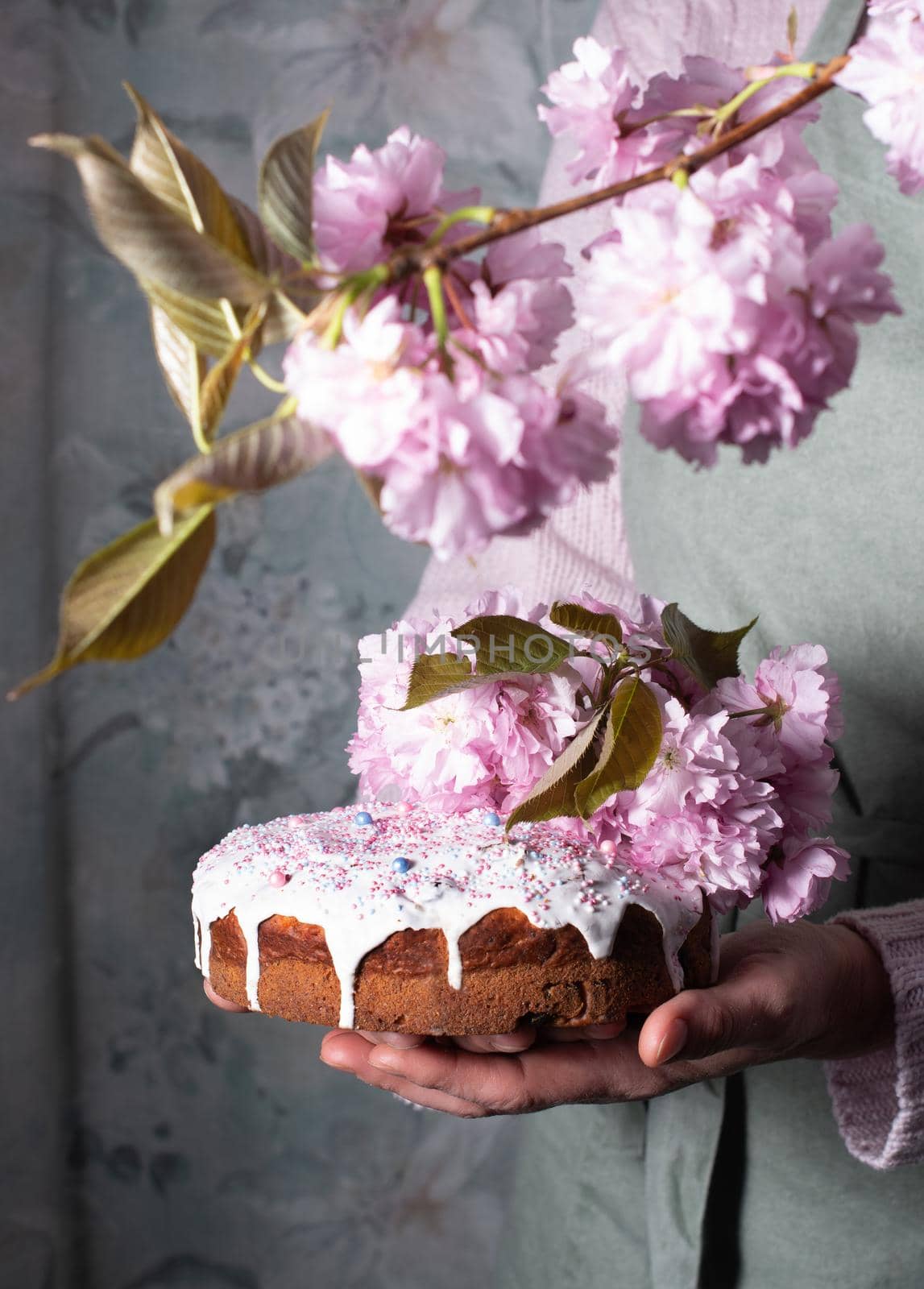 a woman decorates a homemade Easter cake with pink sakura flowers,spring blossom by KaterinaDalemans