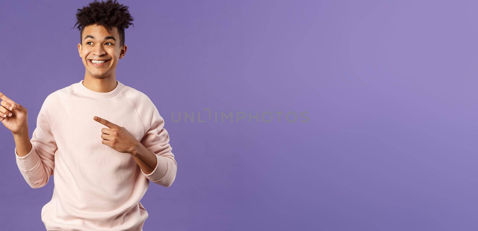 Portrait of enthusiastic, good-looking hispanic man with dreads, looking and pointing upper left corner with satisfied beaming smile, seeing cool thing, made his choice, purple background.