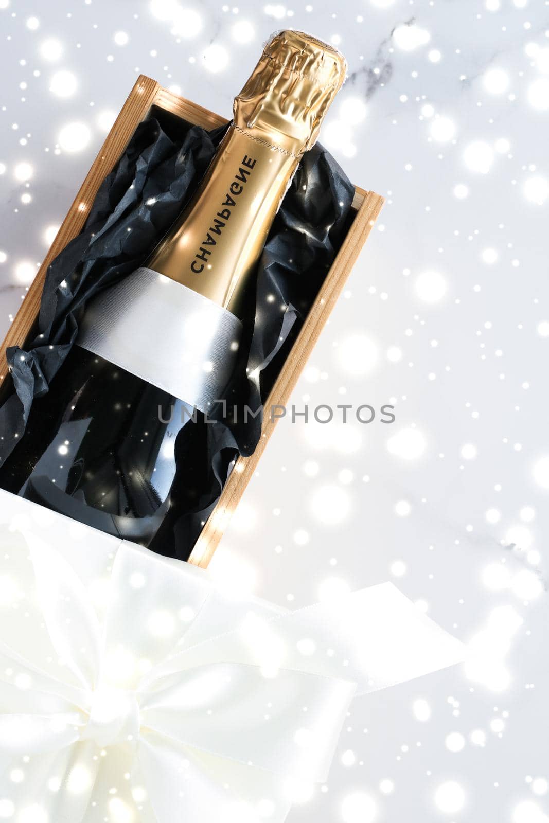 Christmas holiday champagne bottle and a gift box and shiny snow on marble background by Anneleven