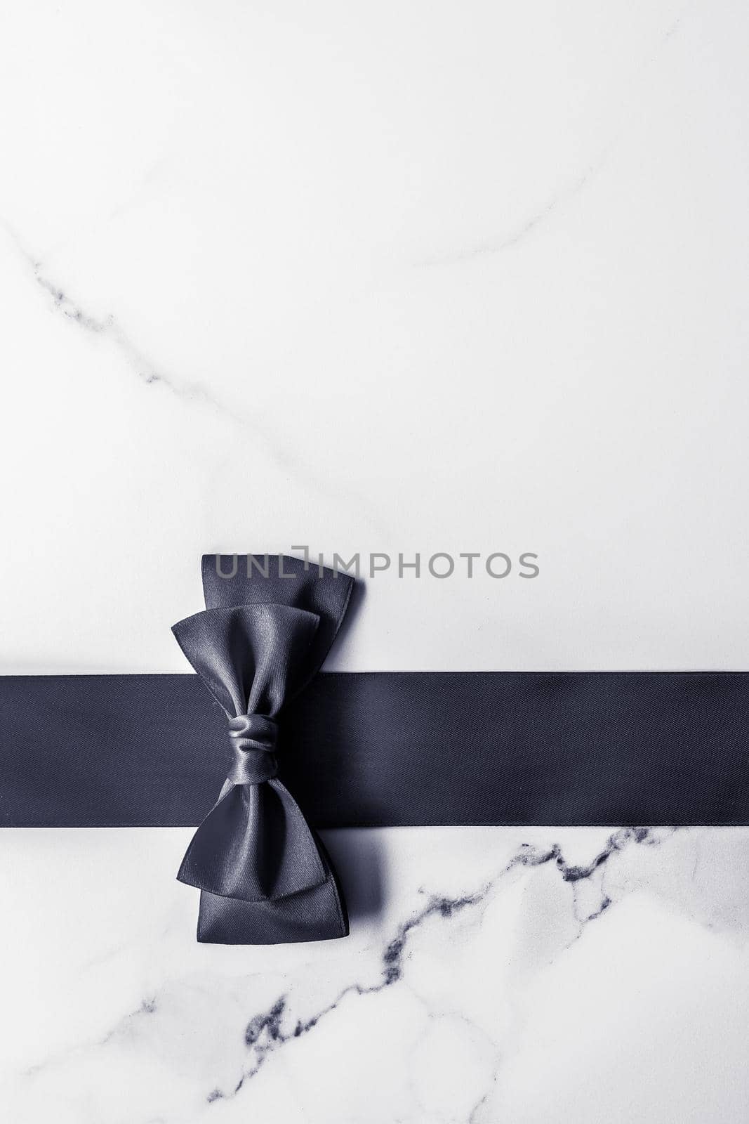 Black silk ribbon and bow on marble background, flatlay by Anneleven