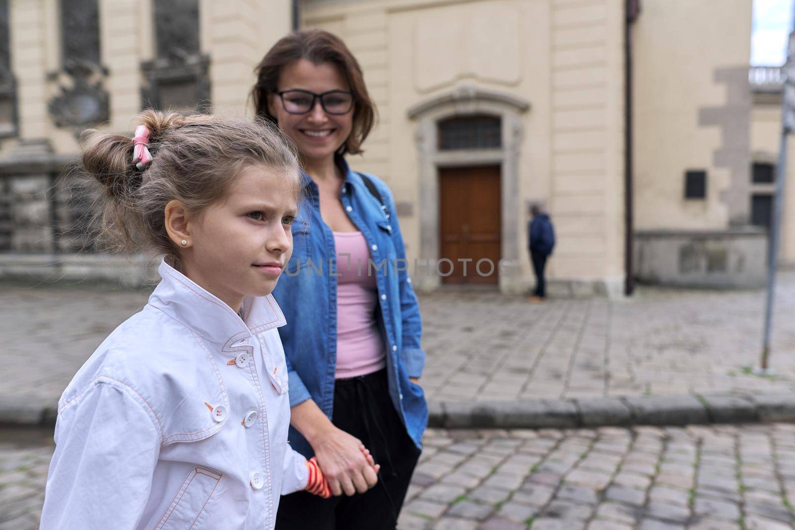 Mother and daughter child 8, 9 years old walking together along street of old city holding hands