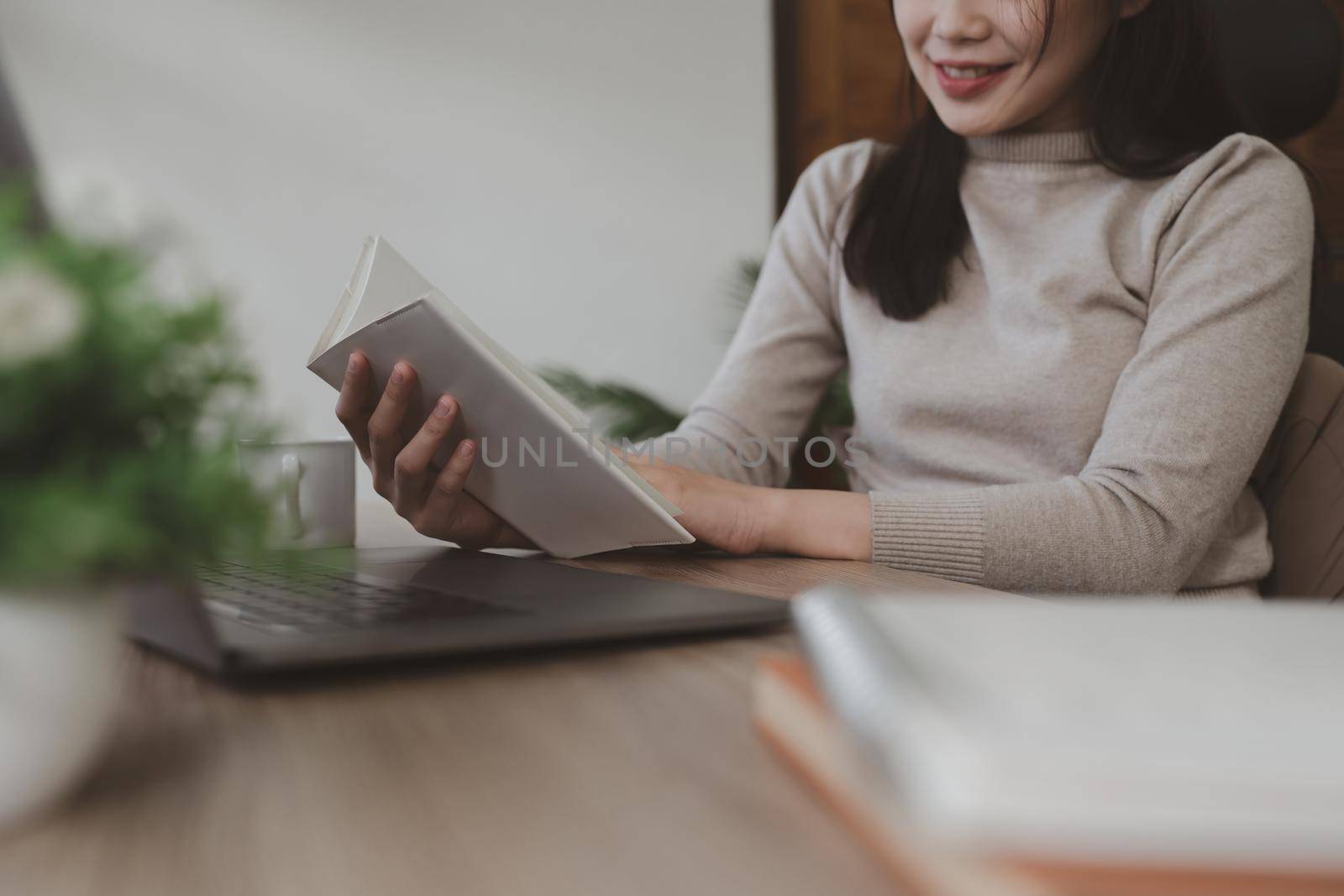 Asian Woman reading a book at her desk at home.