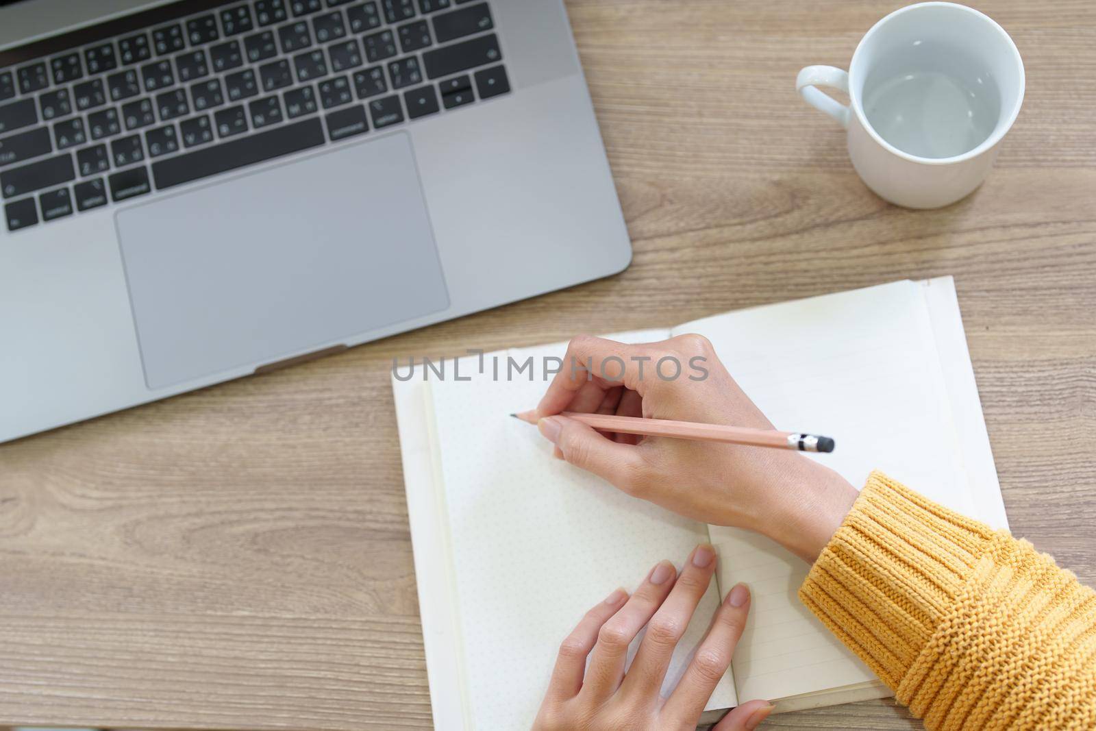 A woman using a pencil to write down memories in a notebook with use computer laptop at home.