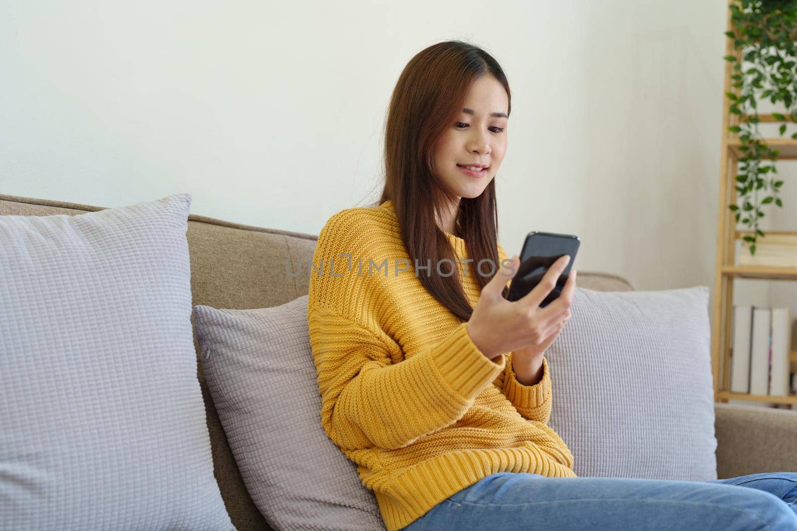 woman sitting on sofa at home ready to use mobile phone by Manastrong