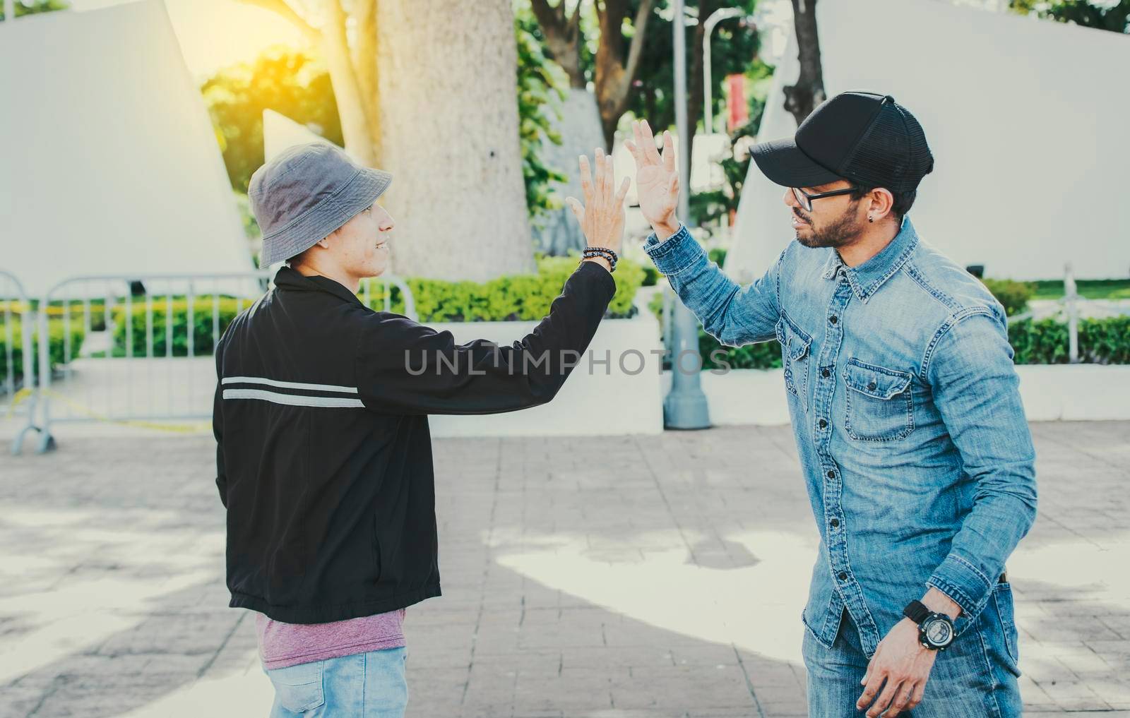 Side view of people greeting each other and shaking hands on the street. Two teenage friends shaking hands outdoors. Concept of two friends greeting each other with a handshake on the street by isaiphoto