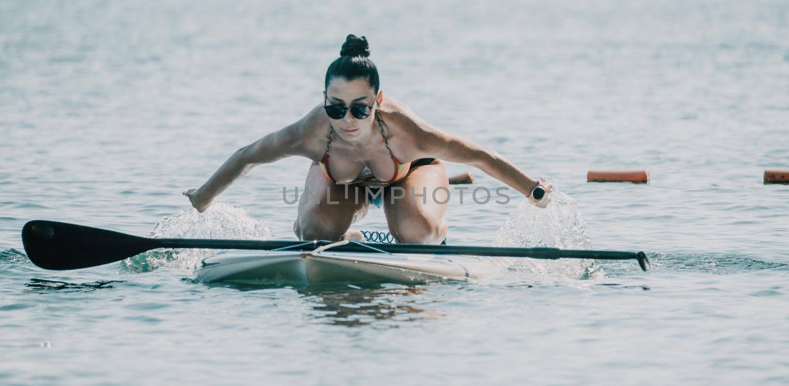 Silhouette of woman standing, surfing on SUP board, confident paddling through water surface. Idyllic sunset or sunrise. Sports active lifestyle at sea or river.