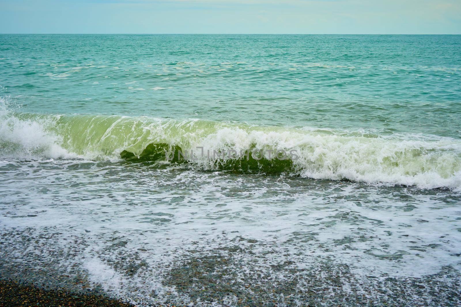 Sea shore with pebbles, wet sea pebbles on the beach and quiet sea surf. Restless sea and waves.
