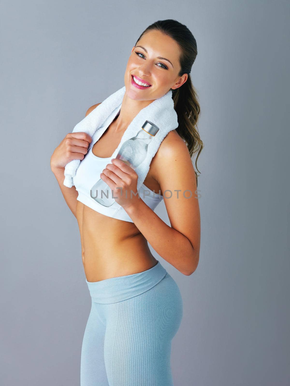 Fit as a fiddle. Cropped portrait of an attractive and sporty young woman holding a water bottle against a grey background