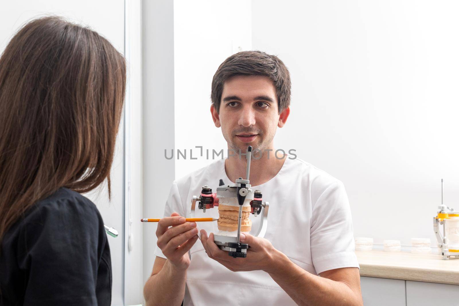 Dentist holding dental articulator with dental gypsum prosthesis model showing it to patient