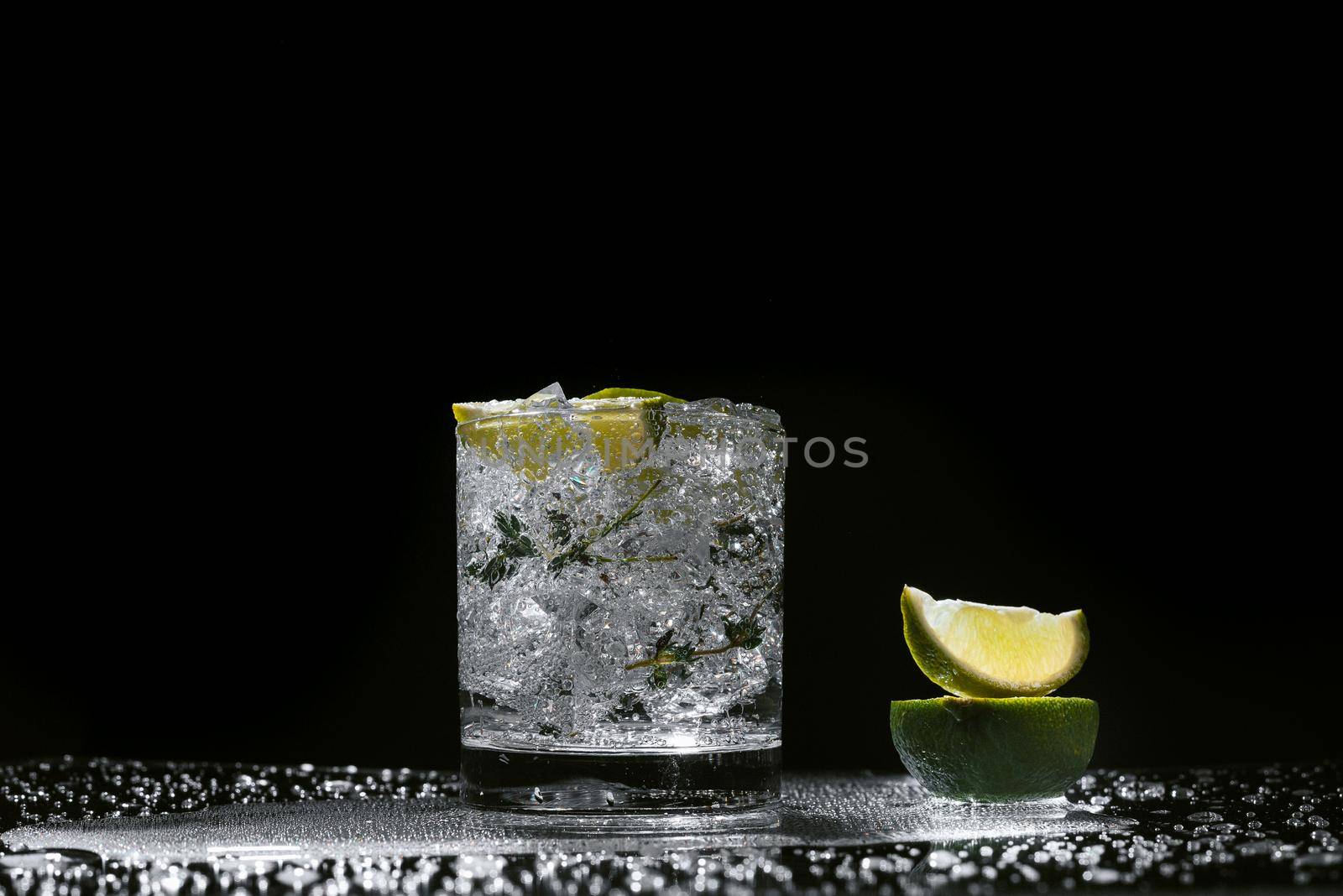 Lime splashing into glass of water on dark background.