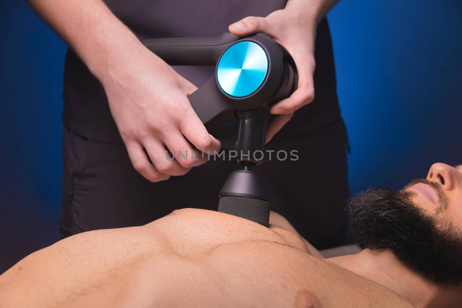 Close-up Sports percussion massage in the medical office of the gym. The masseur makes massage exercises. Percussion therapy for regenerating sports body massage. Sports injury rehabilitation concepts