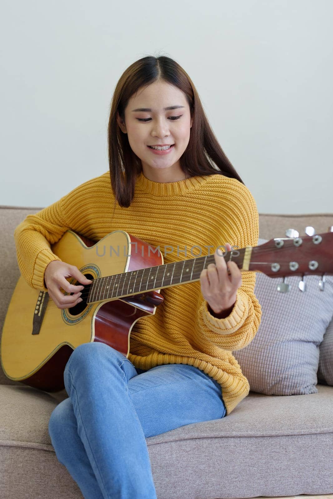 Portrait of a woman playing guitar on the sofa happily in the house.