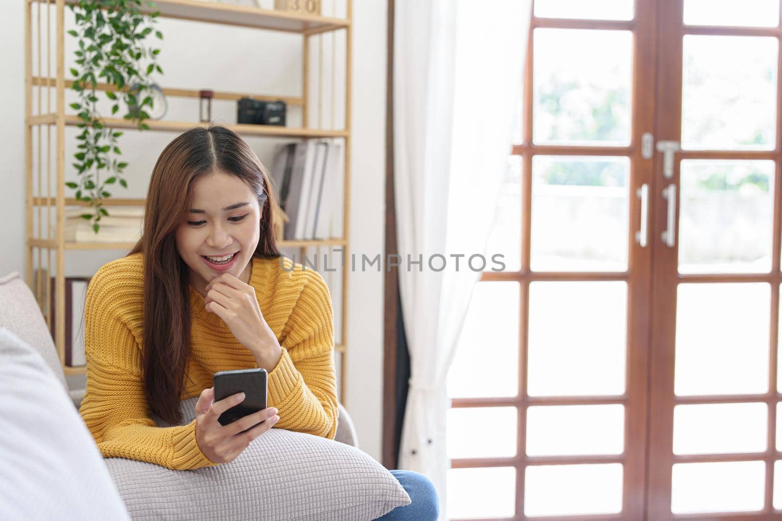 woman sitting on sofa at home ready to use mobile phone by Manastrong