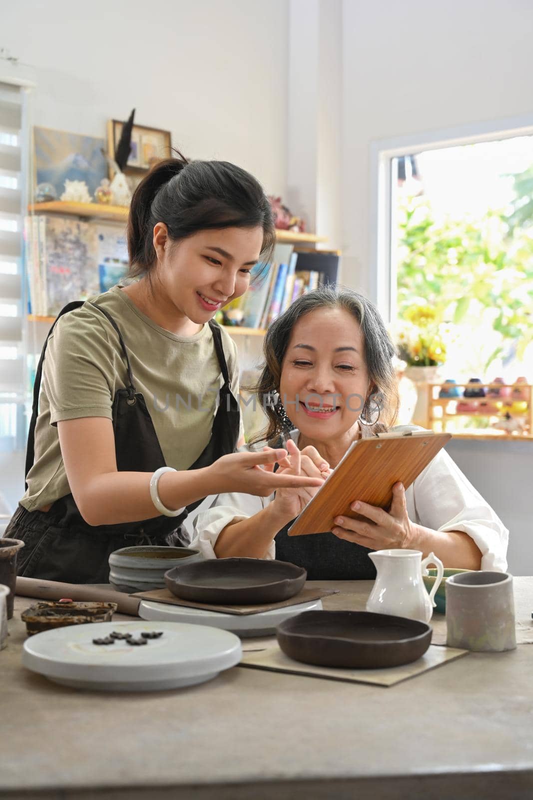 Happy young woman and middle aged woman creating handicraft crockery in workshop. Activity, handicraft, hobbies concept by prathanchorruangsak