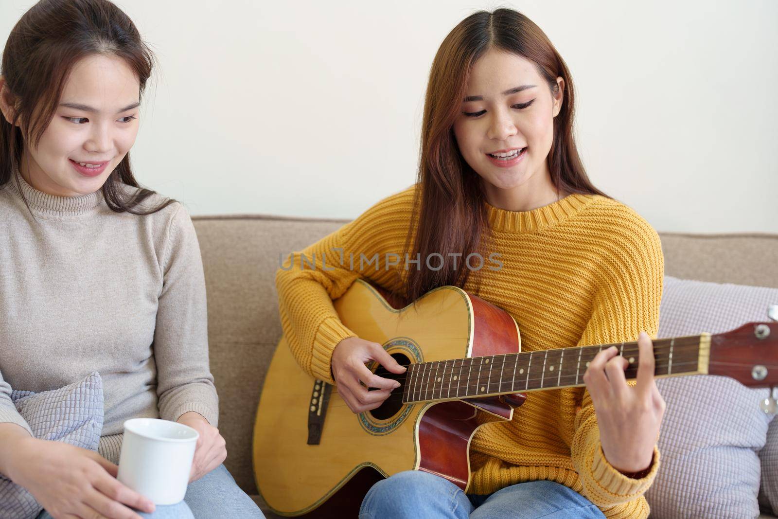 LGBTQ concepts, female couple playing guitar happily on the sofa in the house.