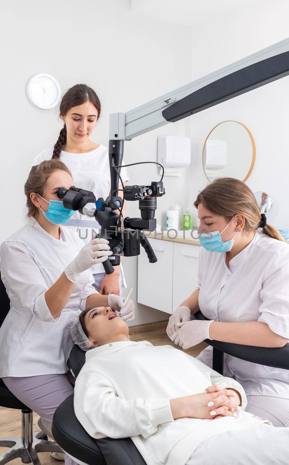 Female dentist using dental microscope treating patient teeth at dental clinic office. Medicine, dentistry and health care concept