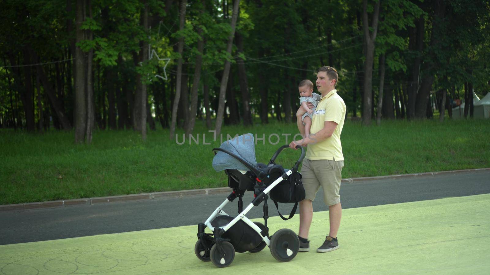 A young dad walks with his son in the park and carries a stroller in front of him. A man with a child in his arms is walking. 4k