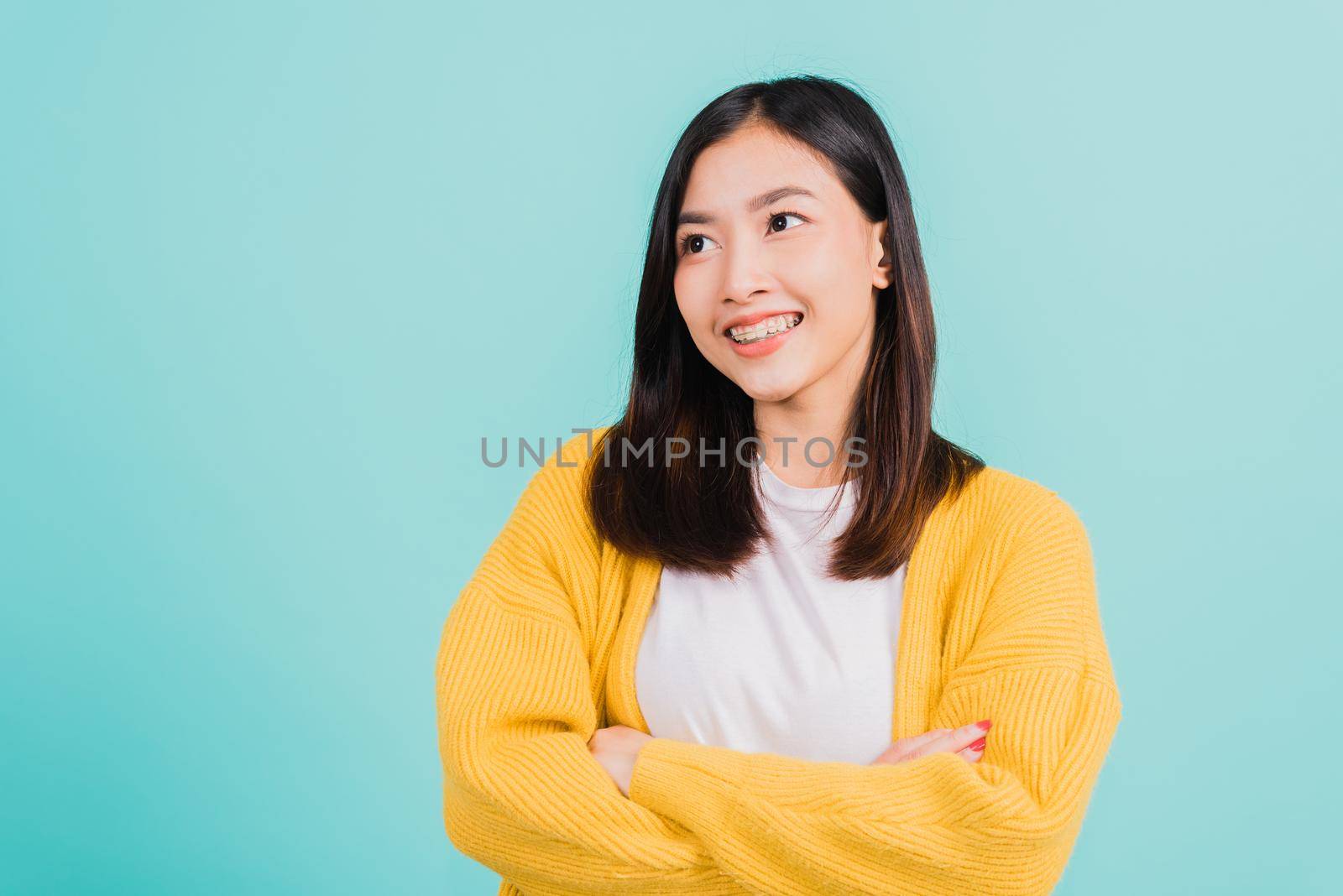 Young Asian beautiful woman smiling wear silicone orthodontic retainers on teeth with crossed arms, studio isolated on blue background, retaining tools after removable braces. Dental hygiene concept