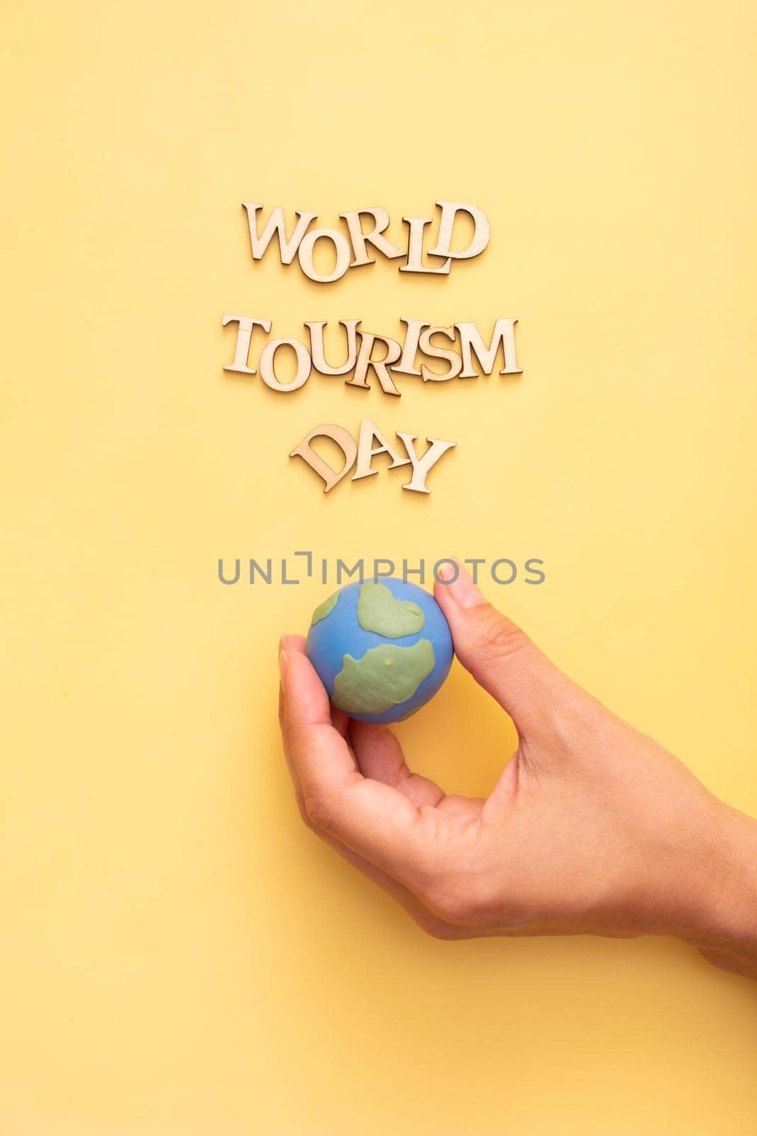 World Tourism Day text from wooden letters on a yellow color background with globe in female hands top view.