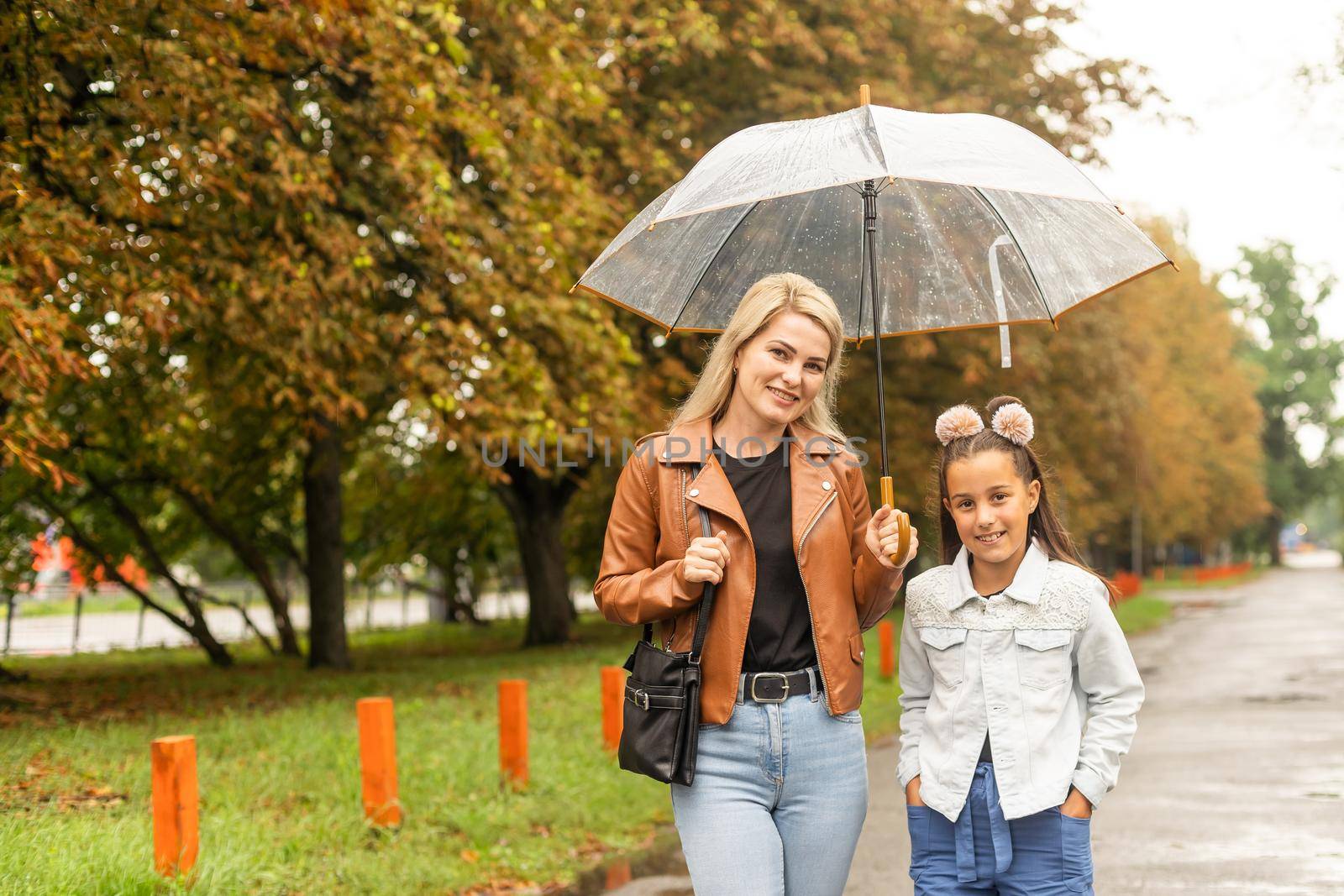 Cheerful mother and her little daughter having fun together in the autumn background under the umbrella. Happy family in the fall background.