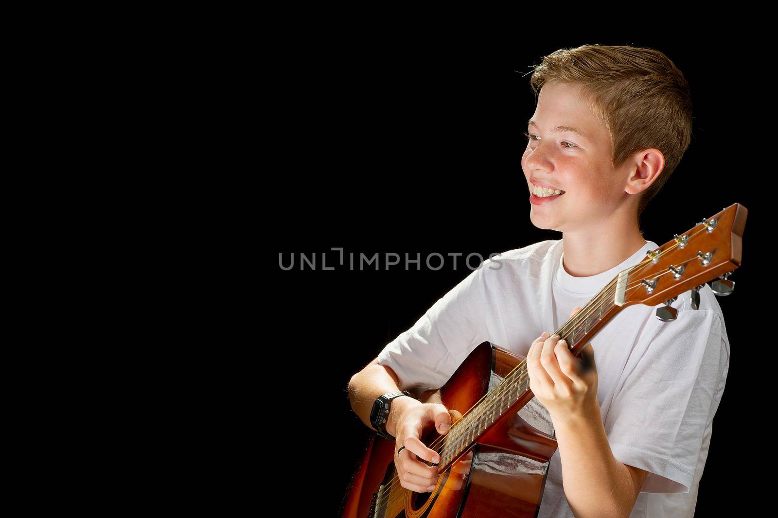 Happy boy playing on acoustic guitar. Teenager boy with classic wooden guitar. boy learning to play guitar on black background. Music education and extracurricular lessons.