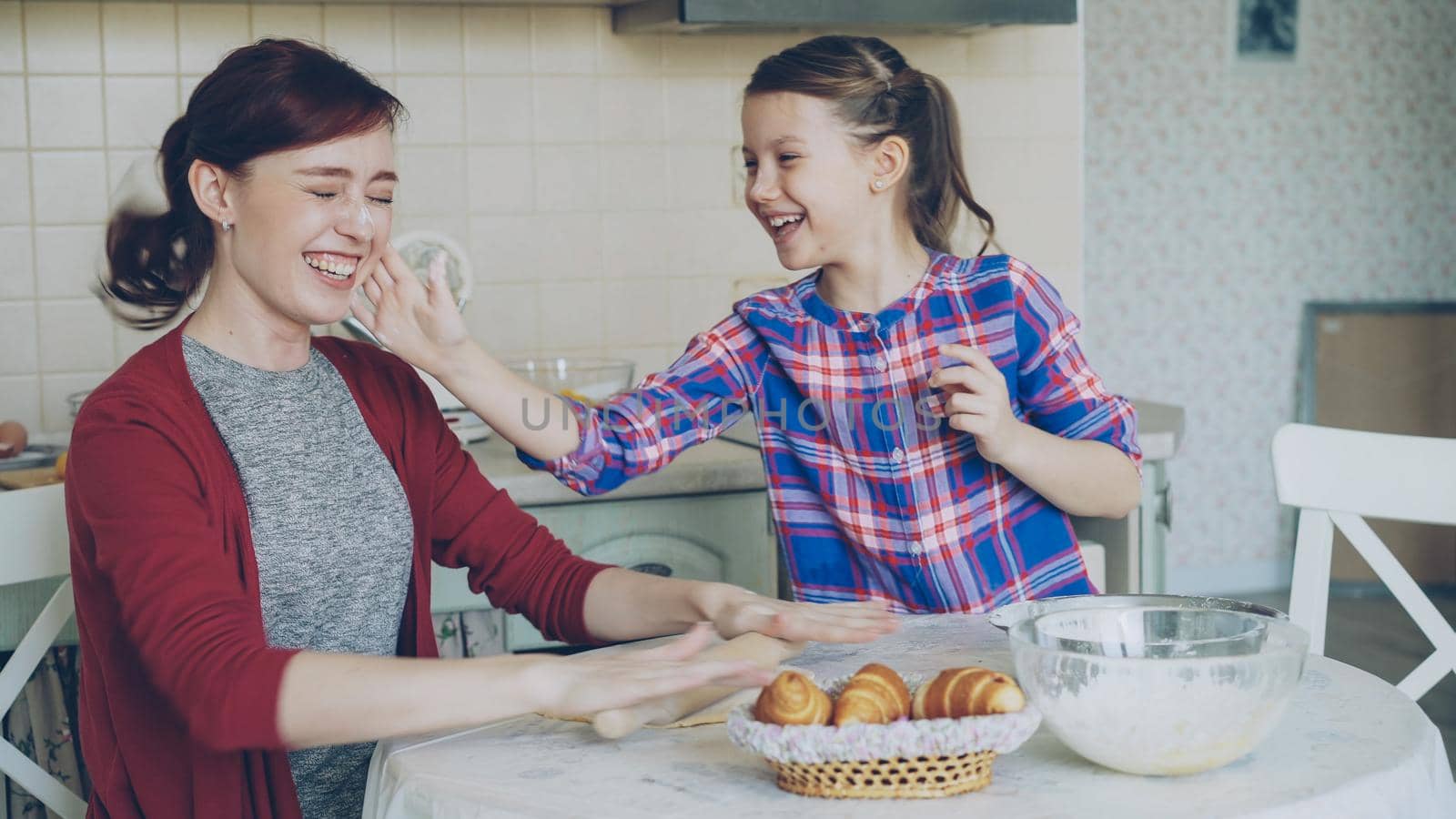 Young mother and her cute daughter have fun smearing nose each other with flour while cooking together in the kitchen on holidays. Family, food, home and people concept