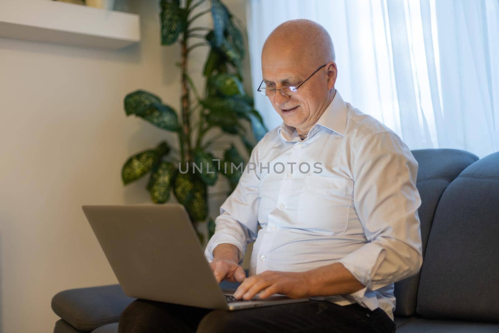 Online teacher with headphones at desk. An elderly man is working on a laptop