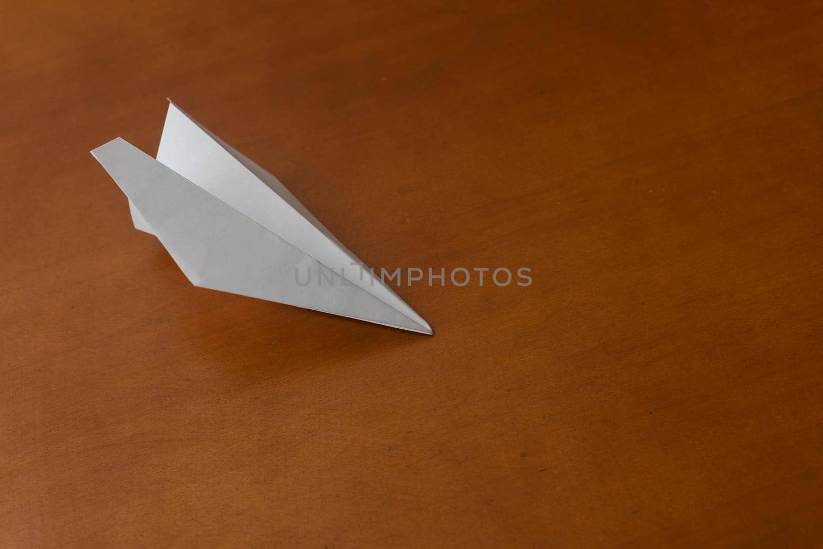 Flat lay of white paper plane on pastel brown background