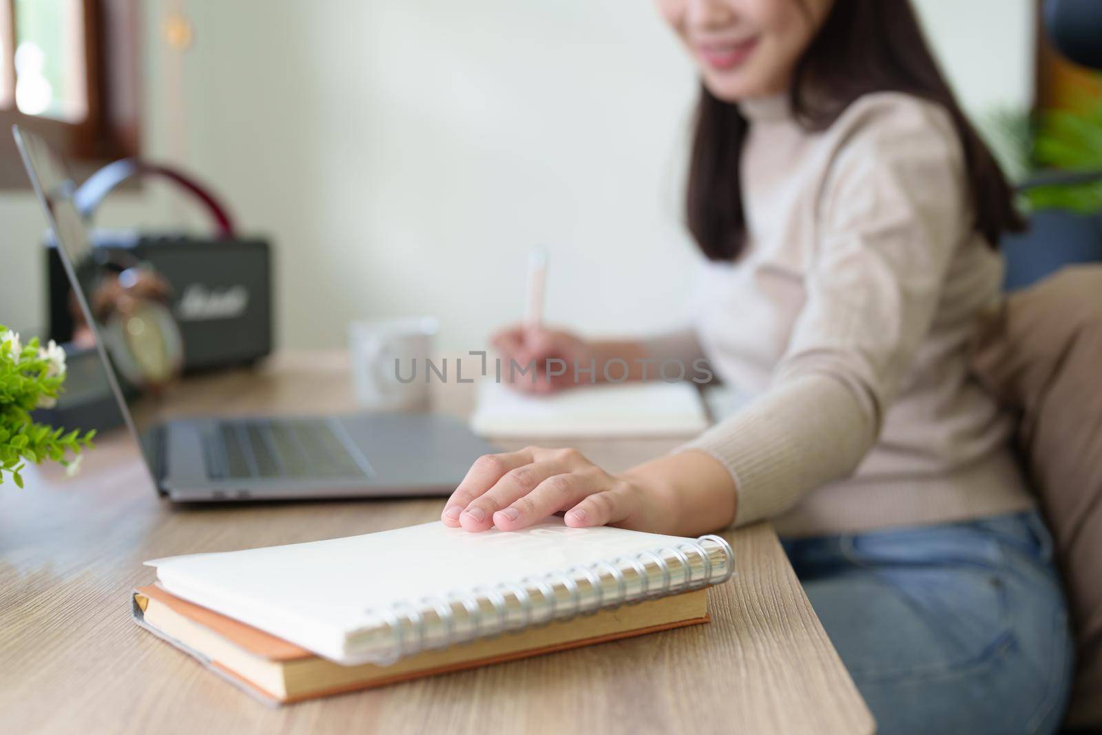 A woman using a pencil to write down memories in a notebook with use computer laptop at home.