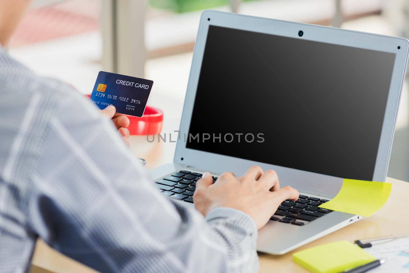 Asian business man hand holding credit card and typing entering security code on a laptop computer for process payment online shopping on the internet at the home office