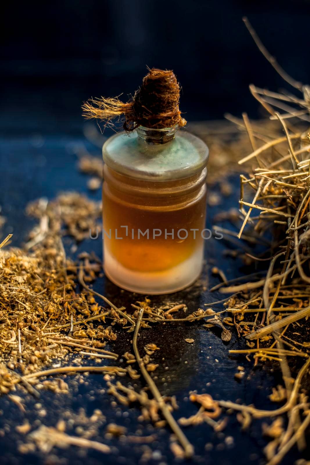 Close up shot of ayurvedic memory booster herb shankhpushpi or Convolvulus pluricaulis roots along with its oil on a black wooden surface with selective focus and blurred background.