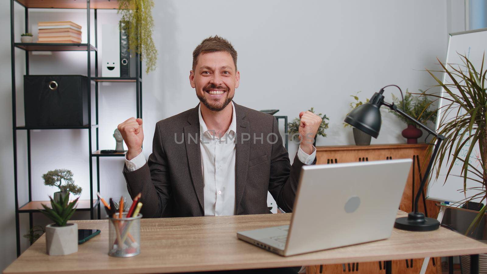 Concentrated businessman winner in suit working on laptop at home office desk typing browsing say Wow yes found out great big lottery win good news celebrate. Male manager freelancer man occupation