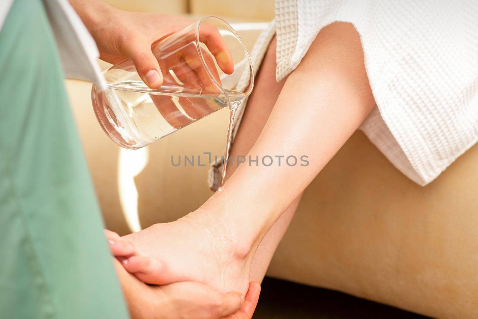 Close up of hands of male therapist washing legs of a young woman in beauty spa salon