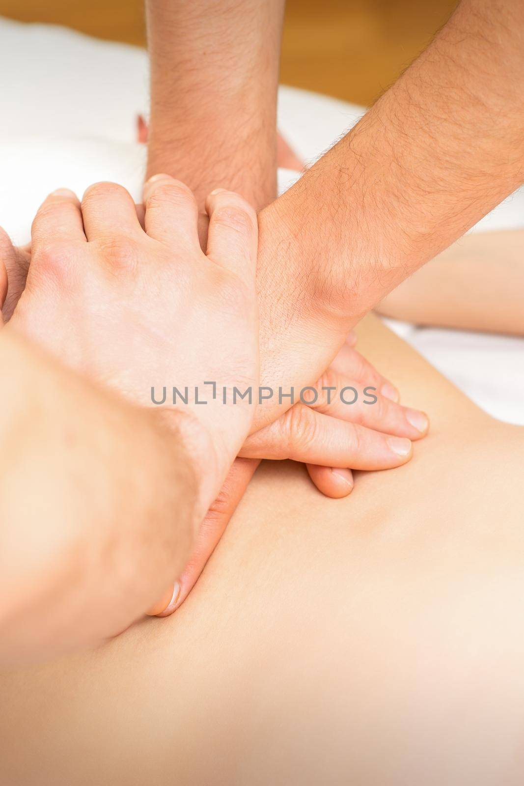 Young woman receiving a back massage in four hands by two masseurs at a spa salon