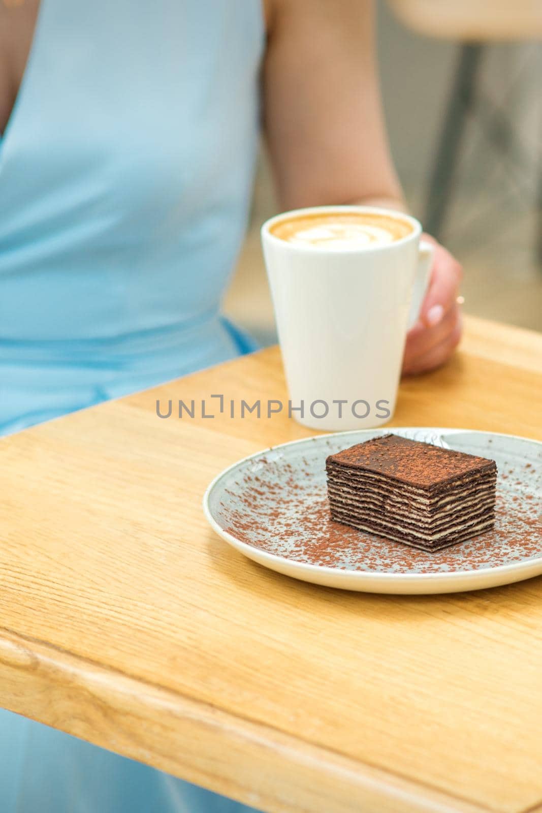 Young woman with cup of coffee and piece of cake sitting at the table in a cafe outdoors