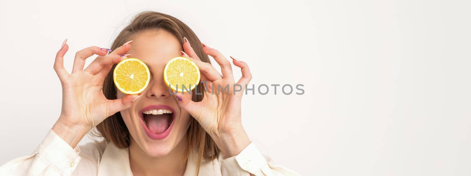 Portrait of a beautiful young woman with an open mouth holding two slices of orange at her eyes against a white background