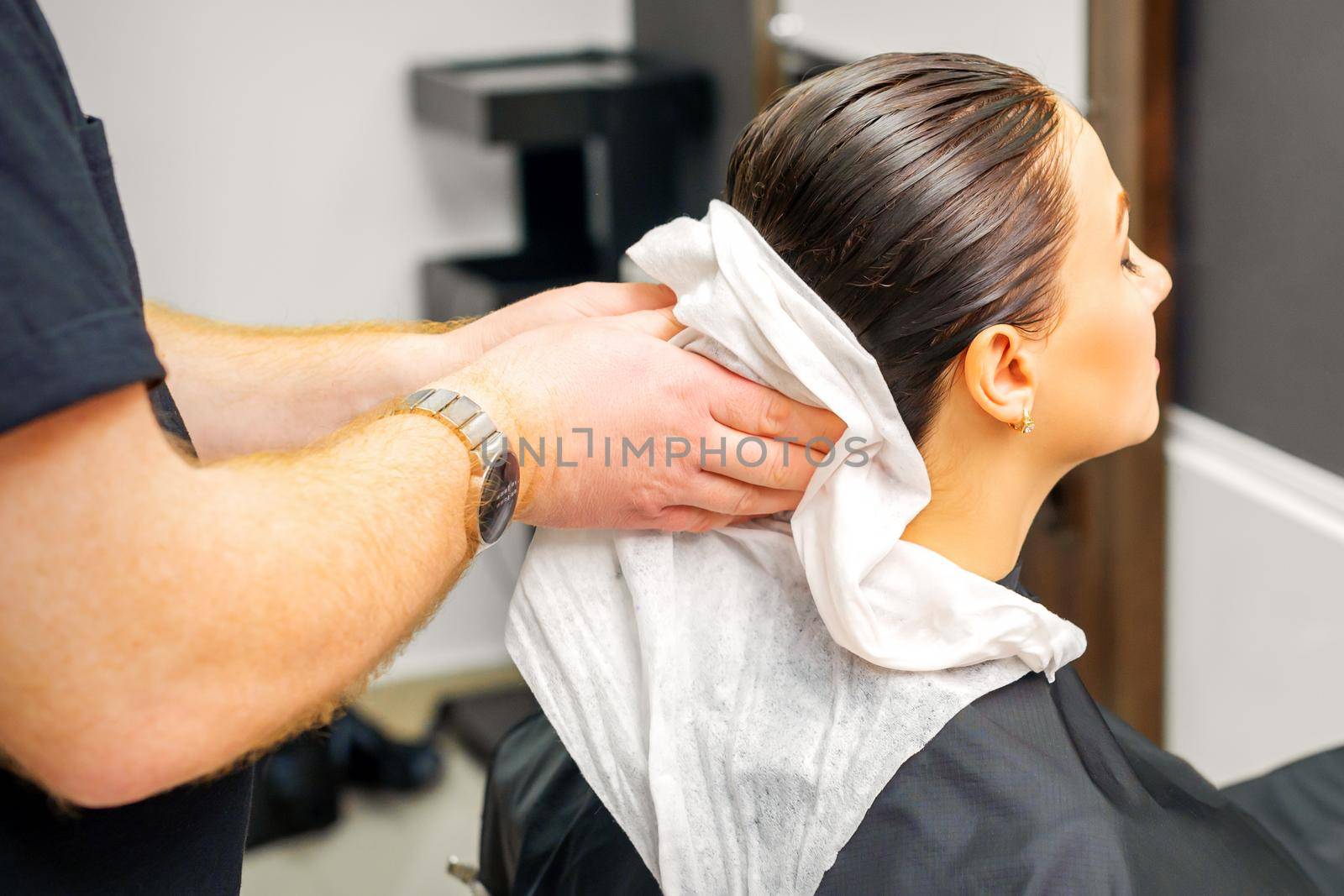 A male hairdresser's hands wipe the hair of a female client with a white towel after shampooing in a beauty salon