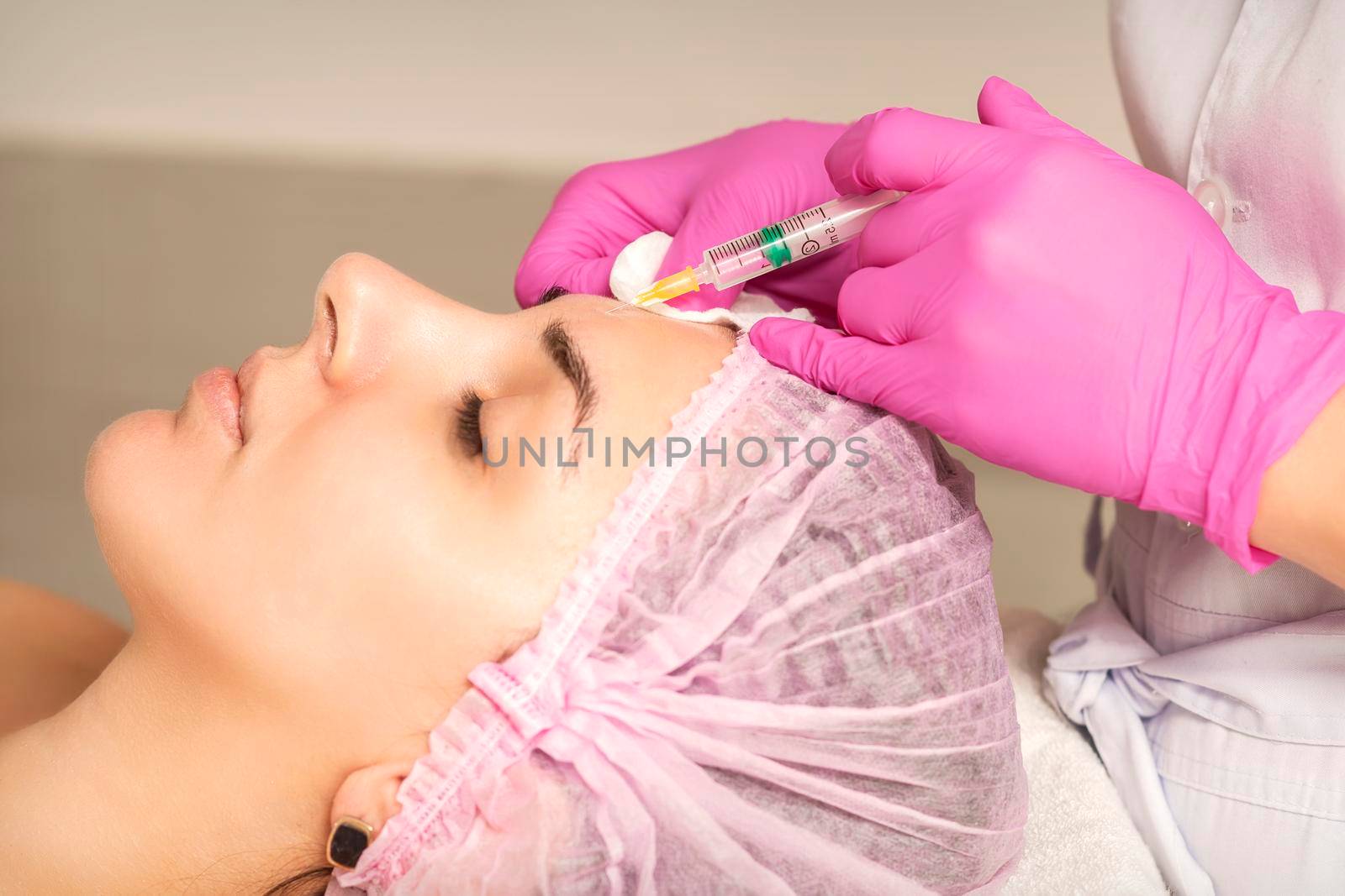 Young woman receiving an injection of anti-aging botox filler to the forehead from a cosmetologist in a beauty salon. Facial treatment injection