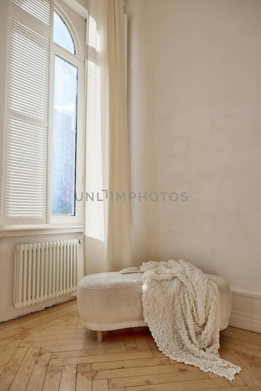 Comfortable ottoman with soft white coverlet placed near window and radiator in light room