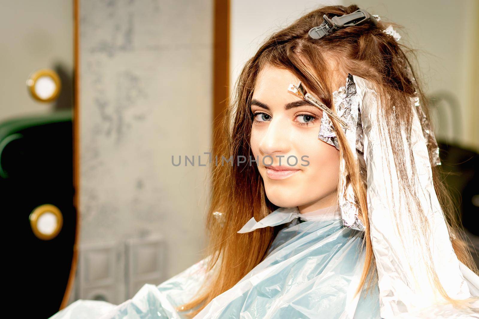 Portrait of a beautiful young caucasian woman getting foil on her hair before dyeing in a beauty salon