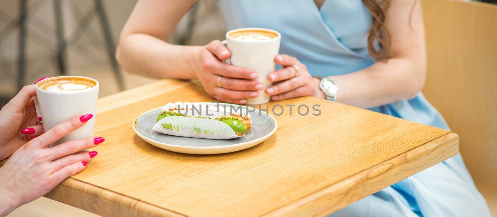 Two young women with cups of coffee and pieces of cake sitting at the table in a cafe outdoors