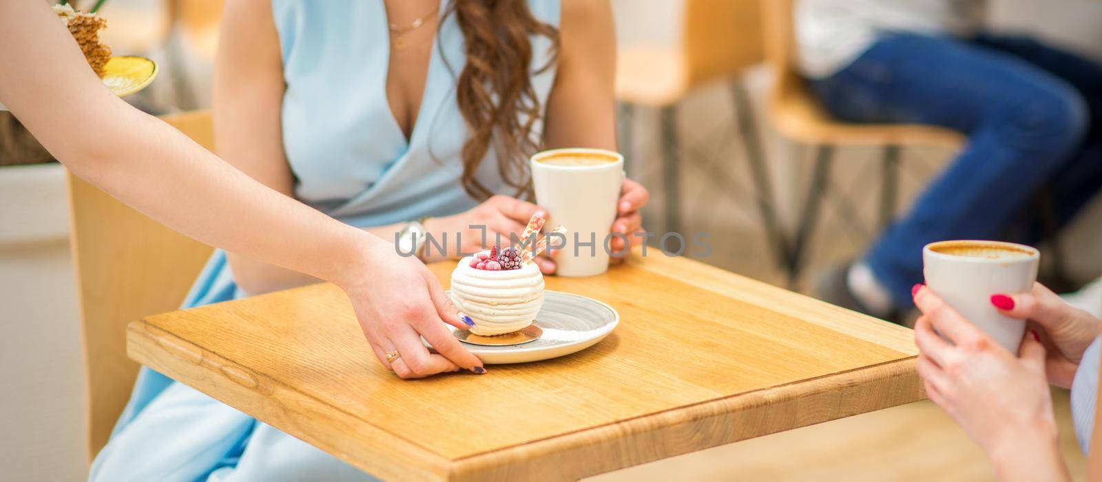 The waitress's hand puts the piece of cupcake on the table at a cafe, woman hand is putting round little pastry on the table on a background of a female in a blue dress
