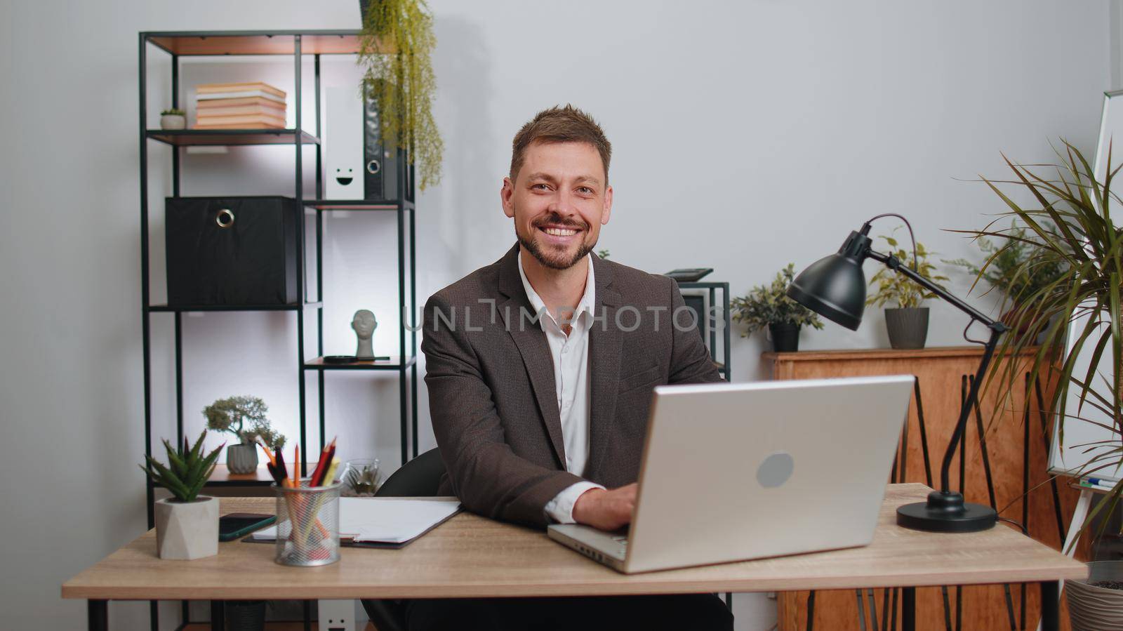 Businessman freelancer in suit enters office workplace, working on laptop computer at desk. Professional manager freelancer man works on notebook, sends messages makes online purchases watching movies