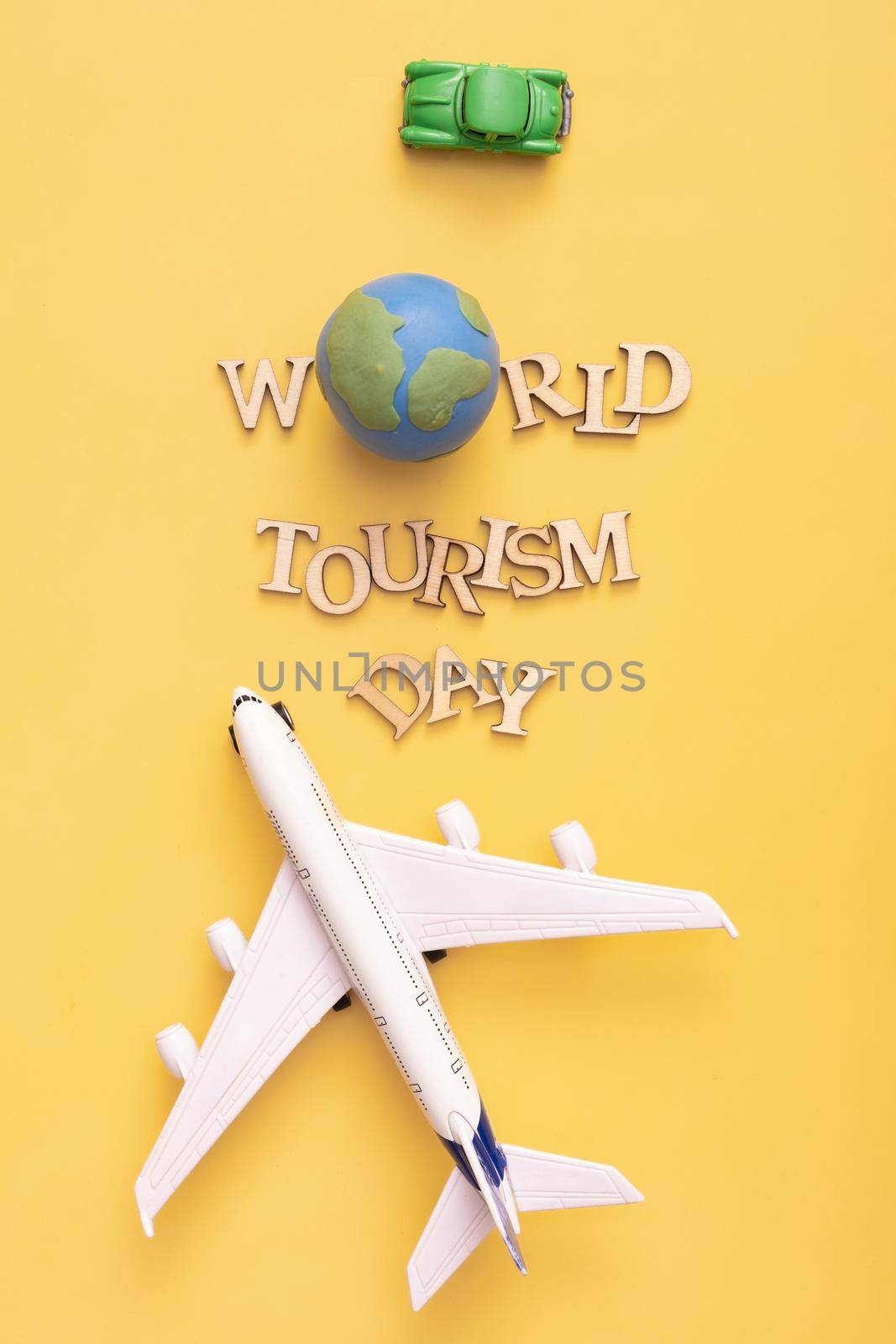 World Tourism Day text from wooden letters with globe, car and airplane on yellow background. Top view, flat lay.