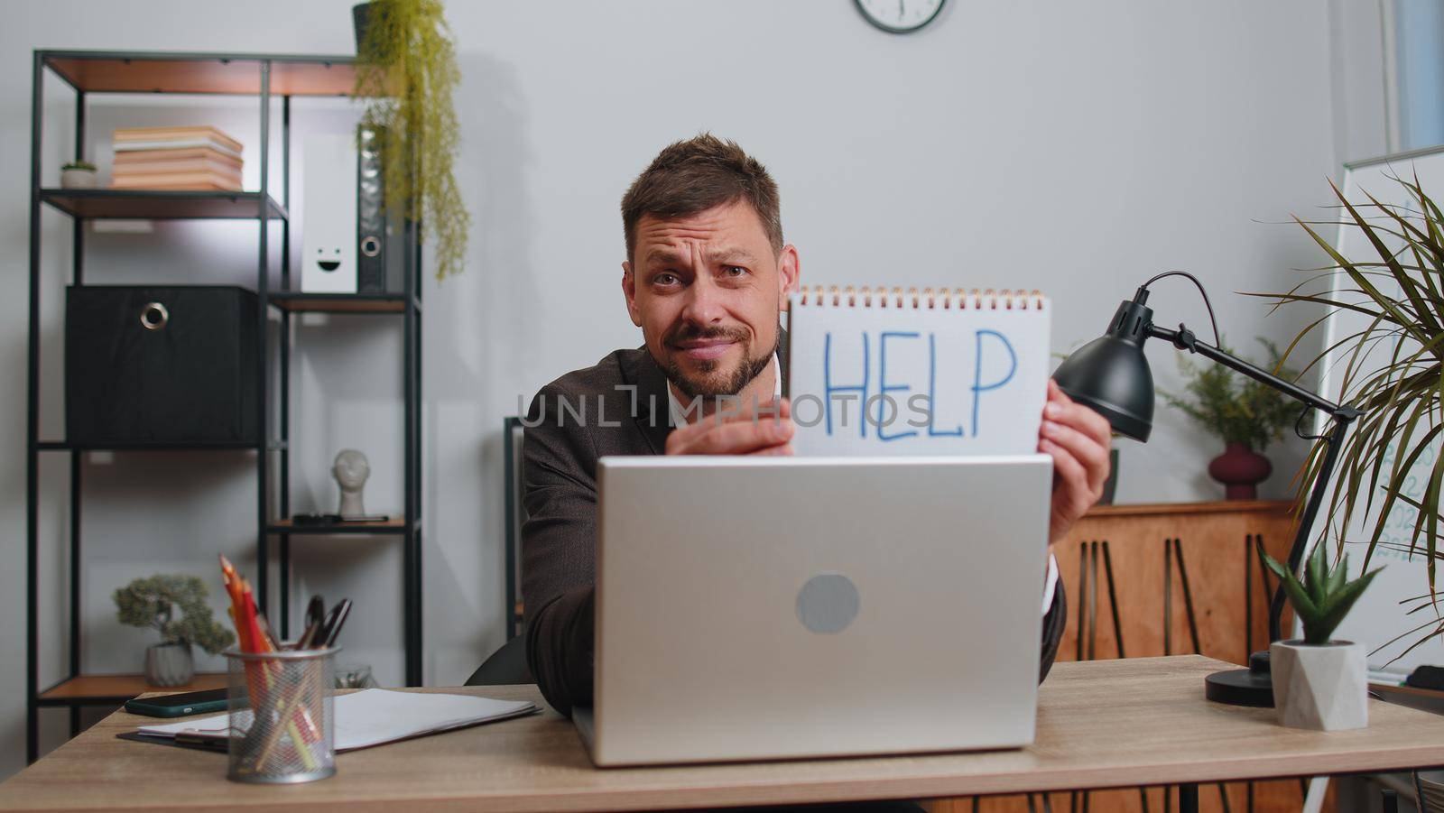 Hopeless sad businessman in formal wear suit working on laptop computer, showing inscription note text Help. Overworked tired freelance business man indoors at office. Poverty, bankrupt, deadline