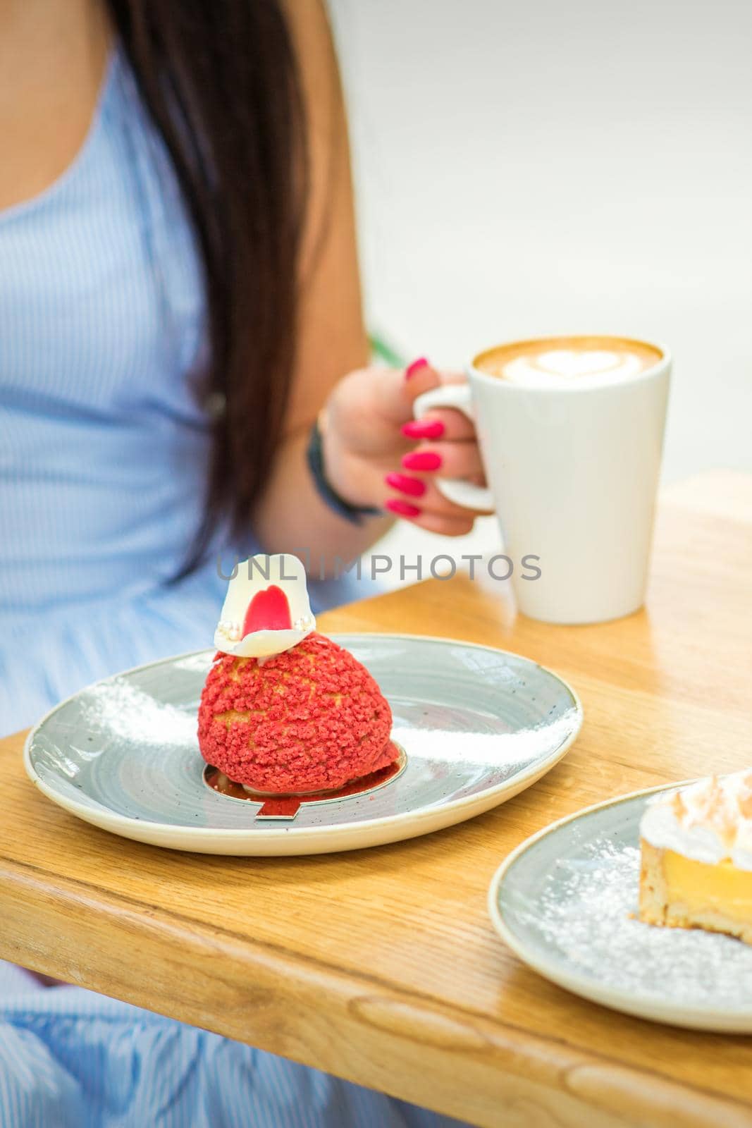 Young woman with cup of coffee and piece of cake sitting at the table in a cafe outdoors