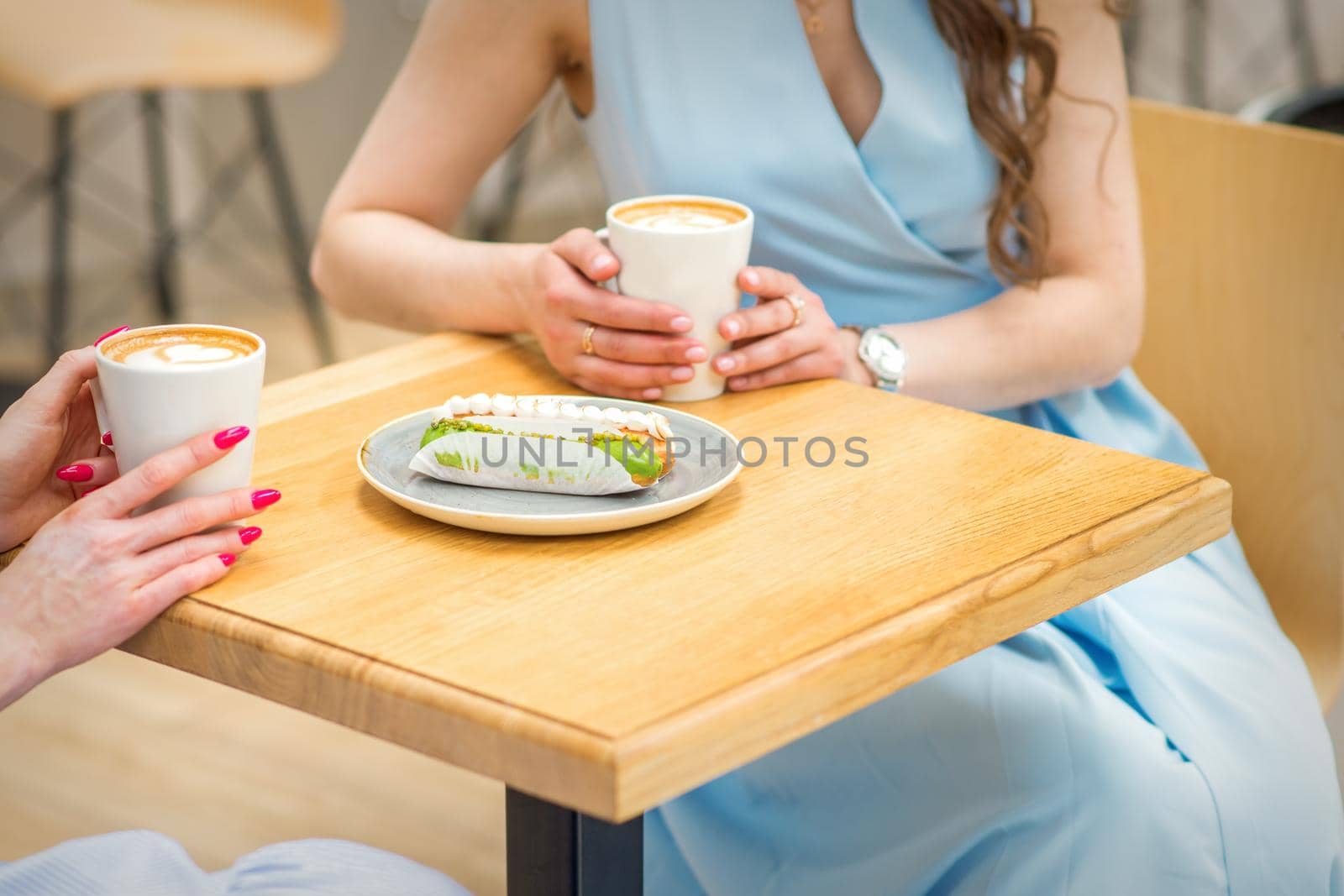 Two young women with cups of coffee and pieces of cake sitting at the table in cafe outdoors
