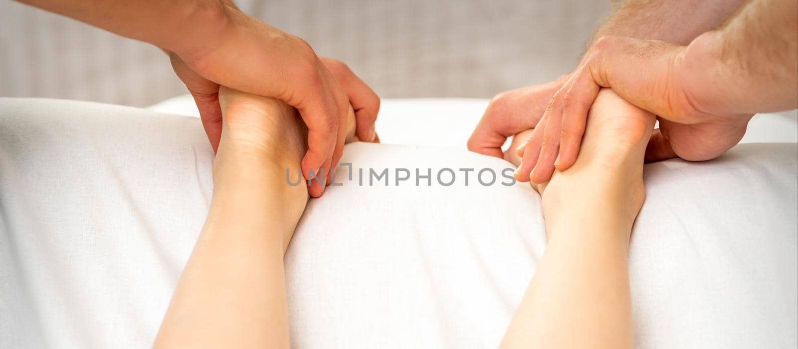 Two masseurs massaging feet of young woman in spa beauty salon